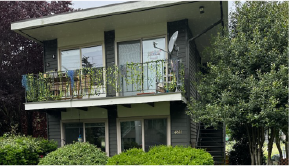 Gray mid century two story apartment building with grass and lovely trees around it. Apartment for rent.