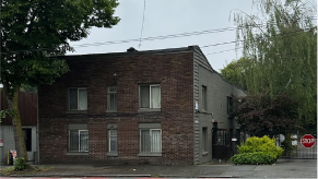 Two story older brick apartment building with big tree in front. Apartment for rent.