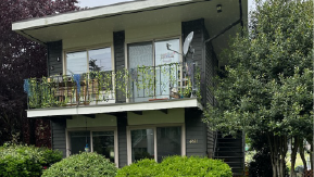 Gray mid century two story apartment building with grass and lovely trees around it. Apartment for rent.